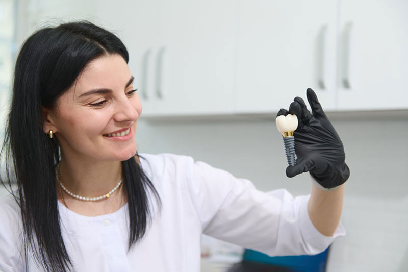 oung woman holding dental implant mockup, artificial tooth roots into jaw canal. dental treatment concept.